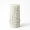 Bougie cylindrique blanche avec relief de sapins enneigés sur fond blanc